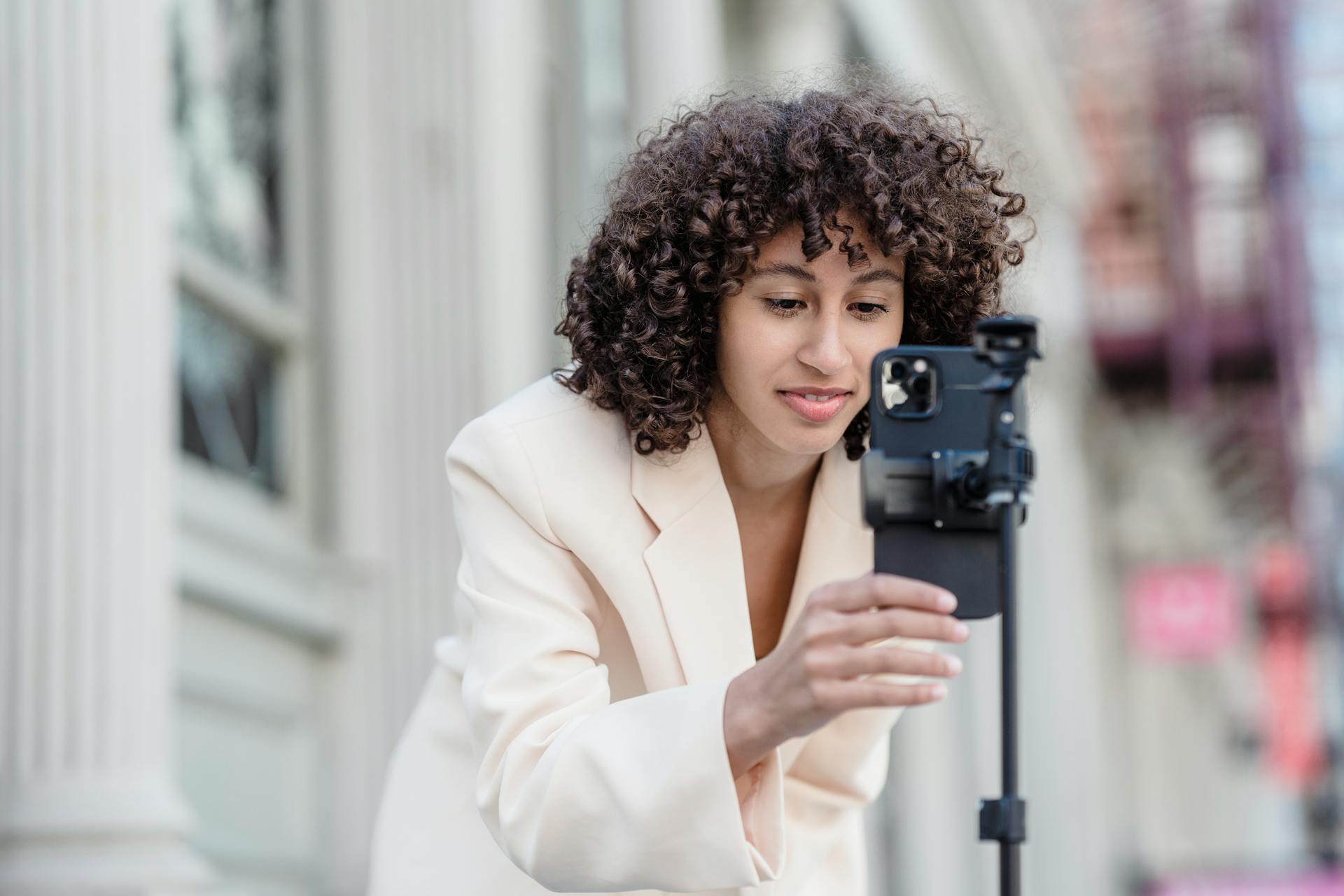 Woman in White Coat Holding a Mobile Phone on a Stand