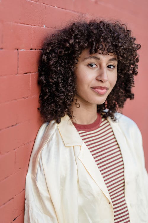 Close-Up Shot of a Curly-Haired Woman Leaning on the Red Wall