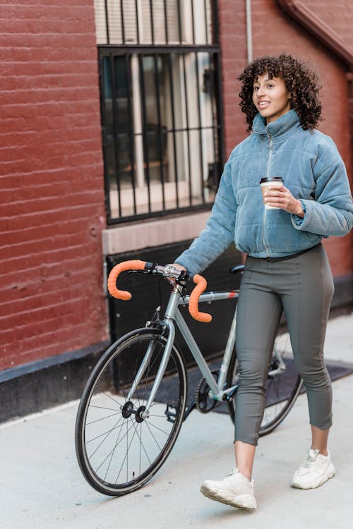 Woman in Blue Long Sleeve Shirt and Blue Denim Jeans Standing Beside Black Bicycle
