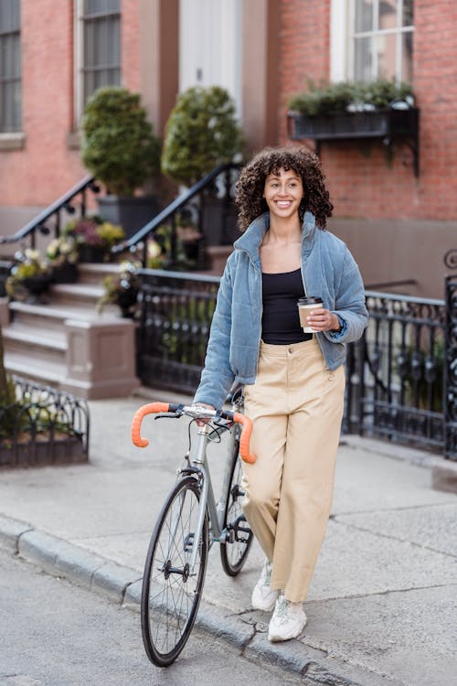 A Woman Walking with her Bicycle while Holding a Coffee Paper Cup