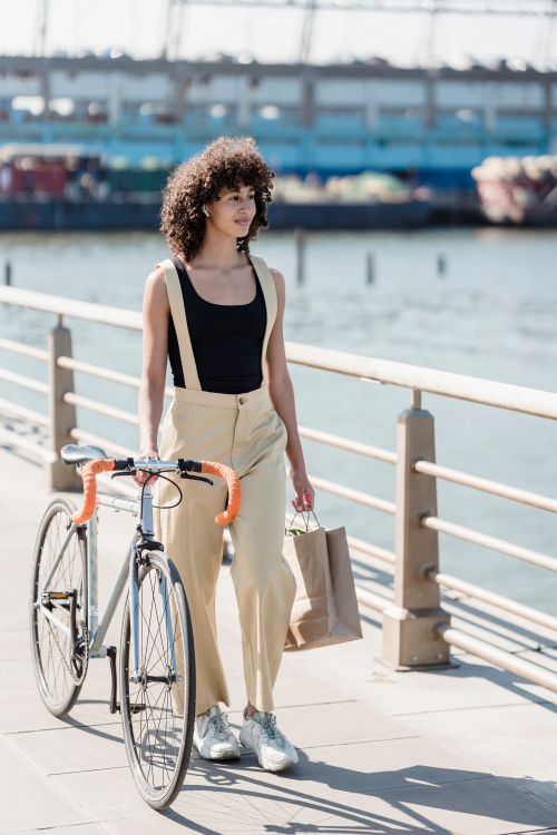 Free Young woman walking with a bicycle along a city waterfront, enjoying a sunny day. Stock Photo