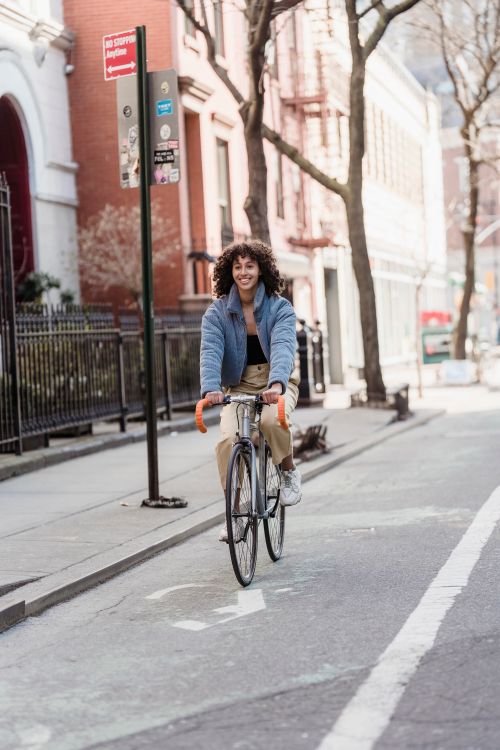 Free Smiling young woman cycling through city streets on a bright day, showcasing vibrant urban lifestyle. Stock Photo
