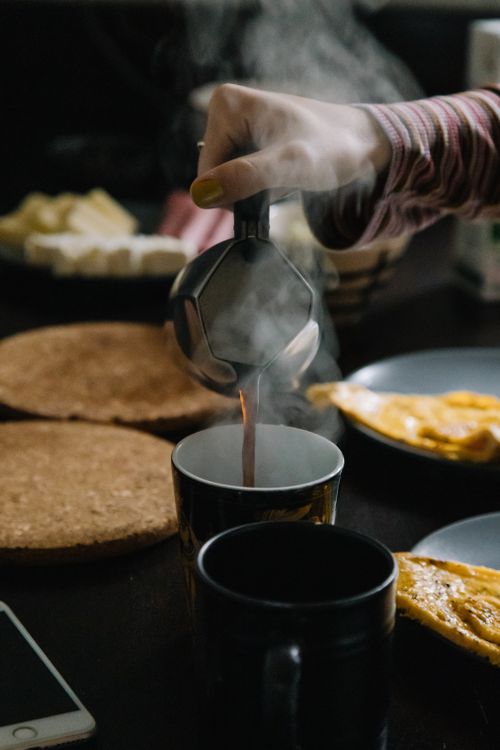 Free Close-up of steaming coffee being poured into a mug, surrounded by breakfast items. Stock Photo