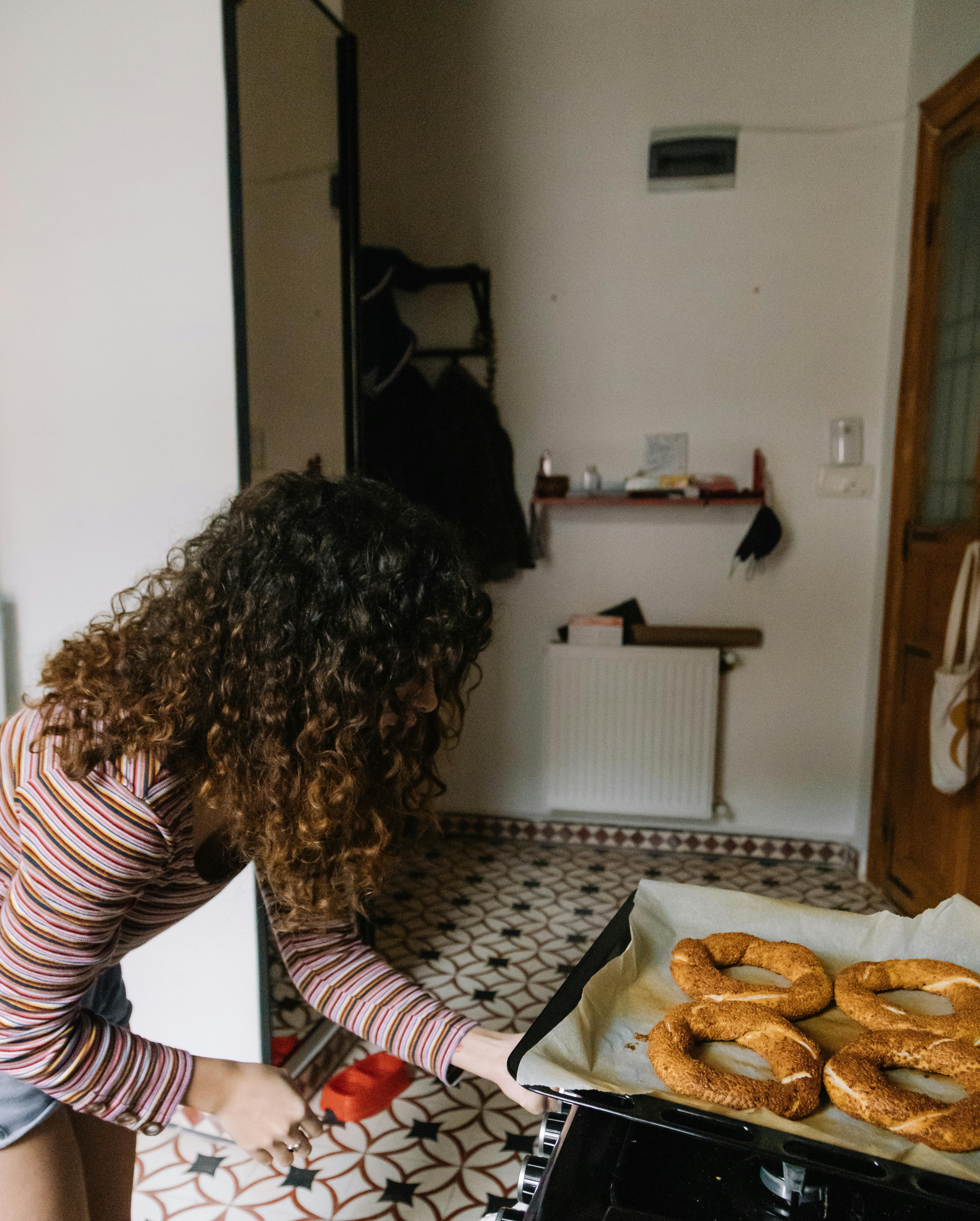 A woman takes freshly baked simit from the oven in a cozy Istanbul kitchen.