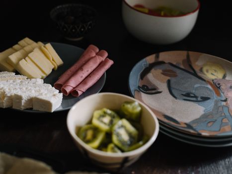 A close-up of a breakfast spread with cheese, deli meat, and sliced kiwi, captured in an artistic setting.