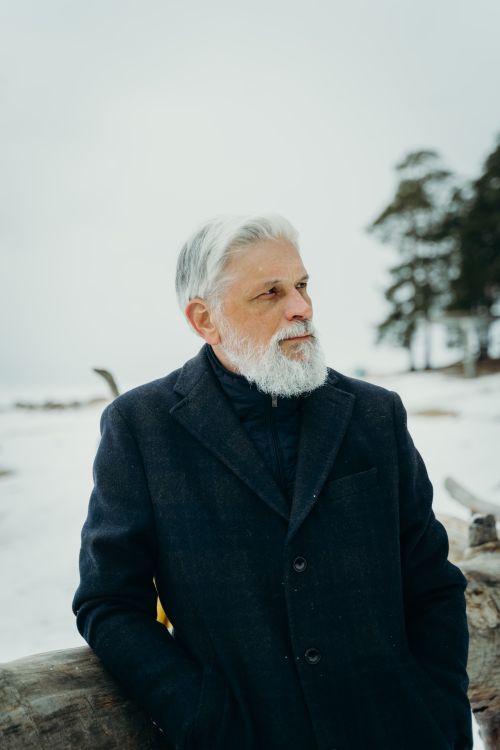 Free Elderly man with white beard standing outdoors in winter, wearing a dark coat. Stock Photo
