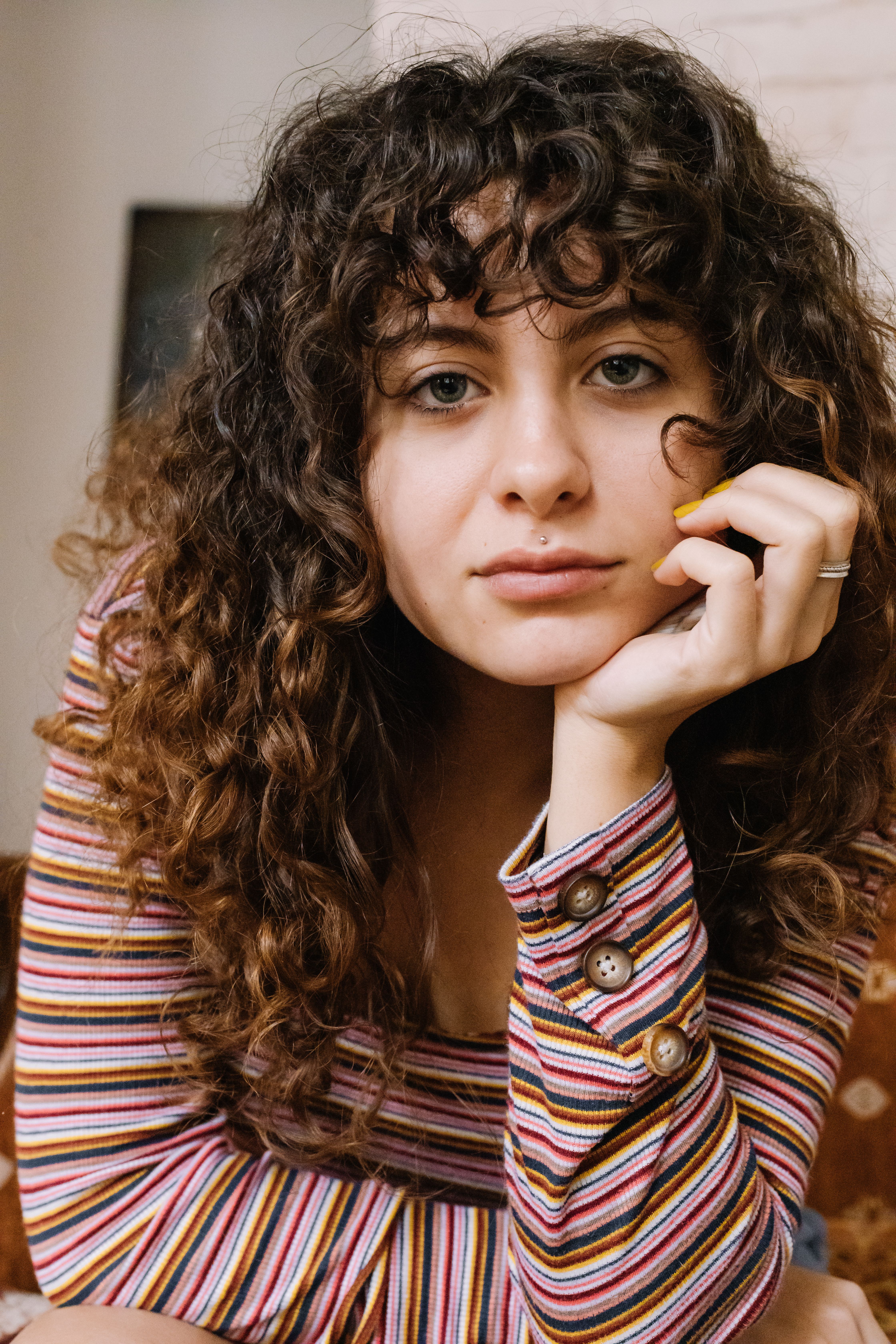 Portrait of a young woman with curly hair in a striped top, looking at the camera indoors.