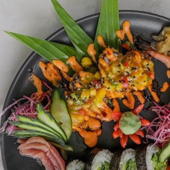 A vibrant sushi platter showcasing fresh fish, vegetables, and artistic presentation on a black plate.