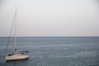 在晴朗的天空下，一艘孤帆静静地漂浮在广阔而平静的海面上