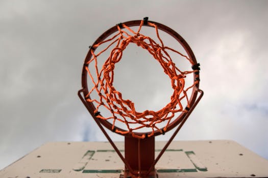 A low-angle shot of a basketball hoop with net against a cloudy sky outdoors.