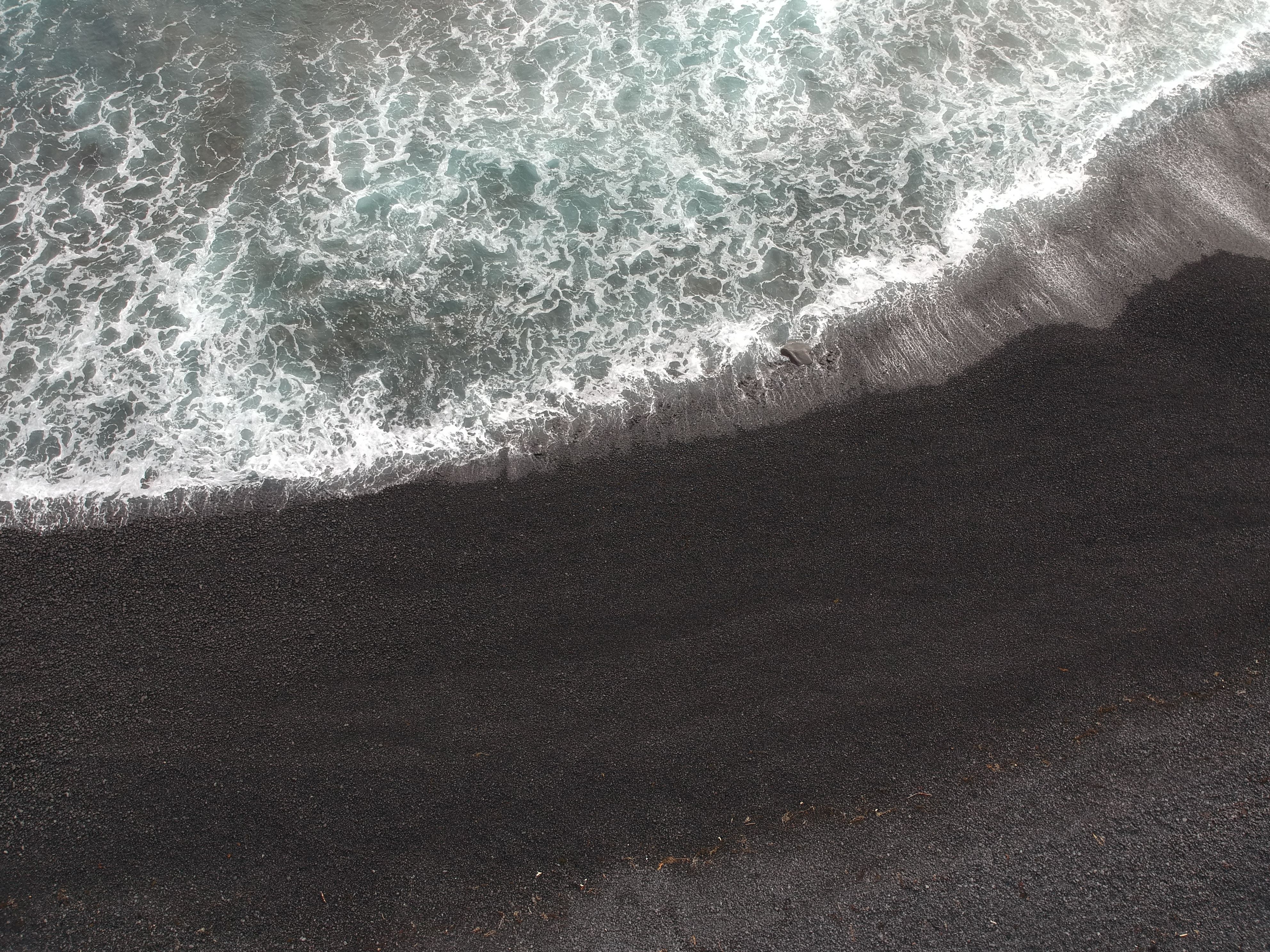 Aerial view of waves crashing on a black sand beach in Iceland, showcasing the natural beauty of the seashore.. pexels, aeria