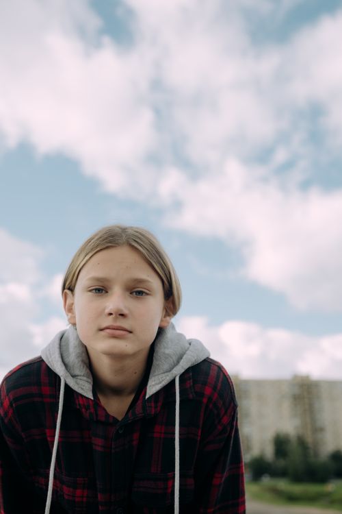 Free Teenage girl outdoors wearing hoodie, cloudy sky background, serene expression. Stock Photo