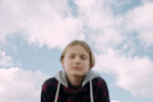 Free A blurred image of a teenager with a cloudy sky background, creating a dreamy effect. Stock Photo