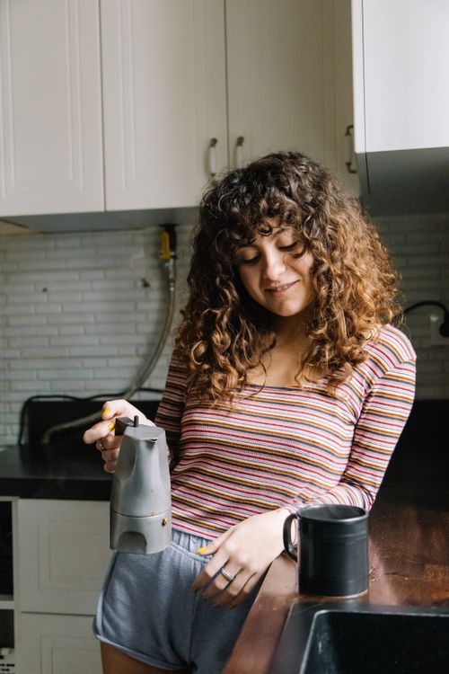 Free Young woman enjoying a morning coffee routine in a cozy kitchen setting. Stock Photo