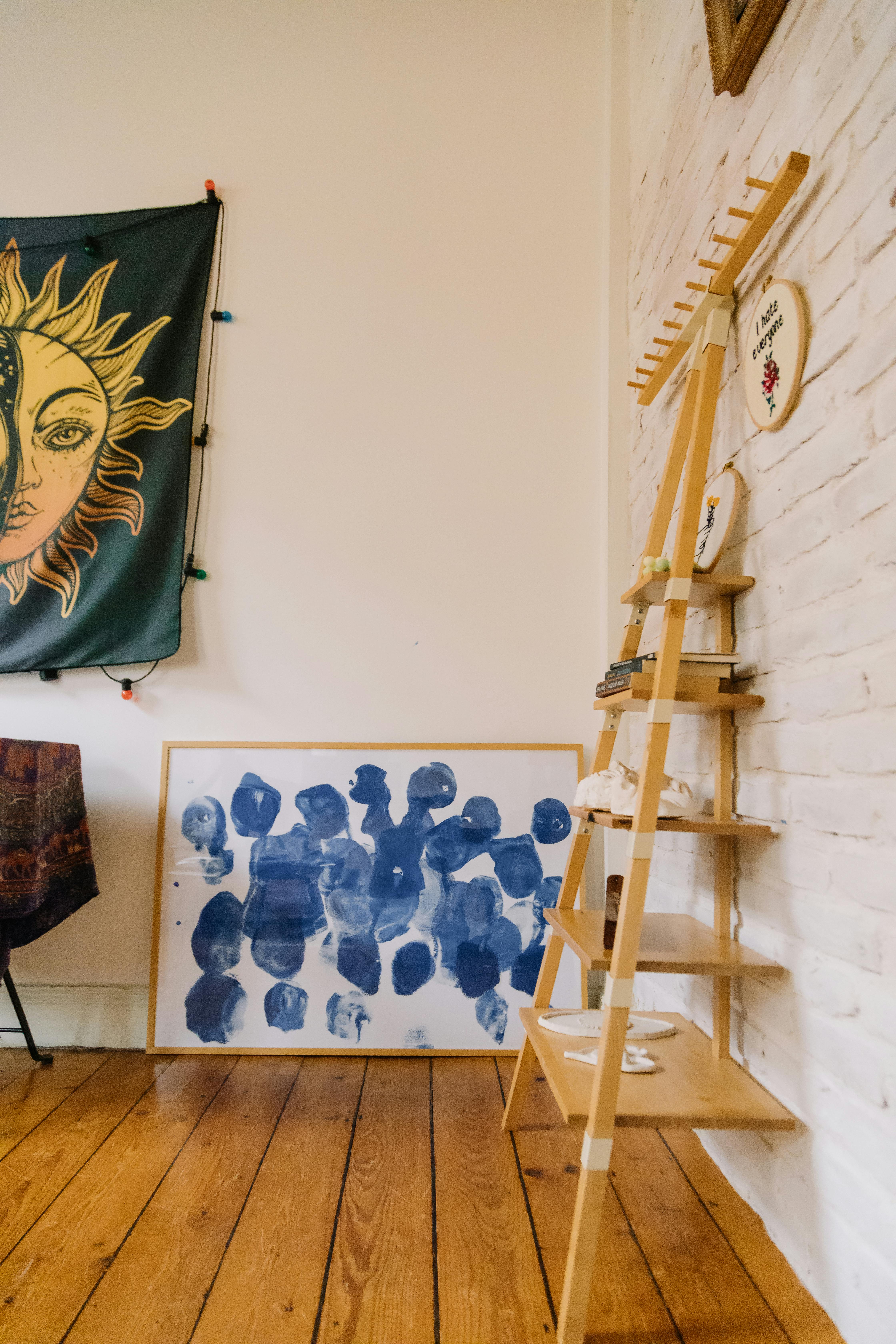 Free A creative indoor space featuring a ladder shelf, abstract artwork, and sun-themed tapestry on display. Stock Photo