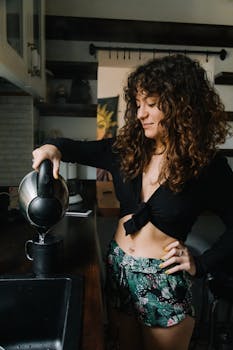 A woman with curly hair pours hot water into a mug in a cozy Istanbul kitchen.