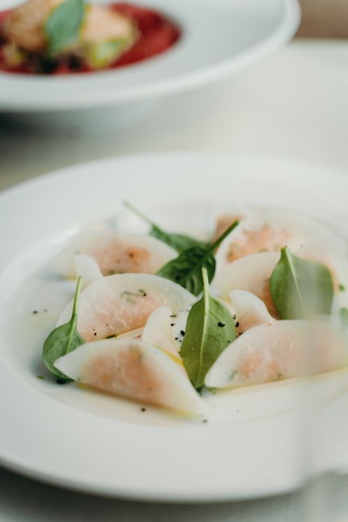 Free A close-up of dumplings garnished with basil leaves on a white plate, showcasing a gourmet meal. Stock Photo