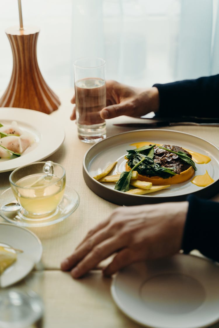 A Person Sitting At A Dining Table With Drinks And Food