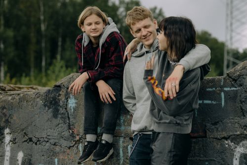Free Three teenagers chatting on a stone wall in a relaxed outdoor setting. Stock Photo