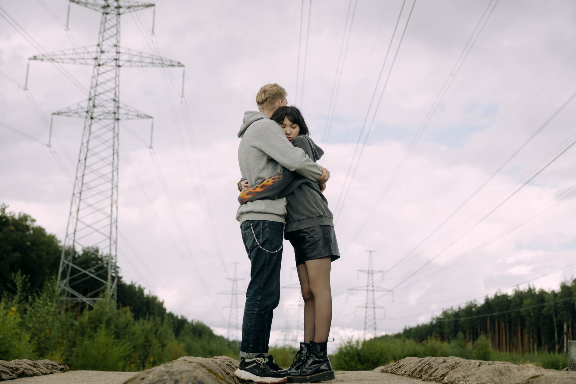 A couple shares a tender hug outdoors beneath towering power lines on a cloudy day.