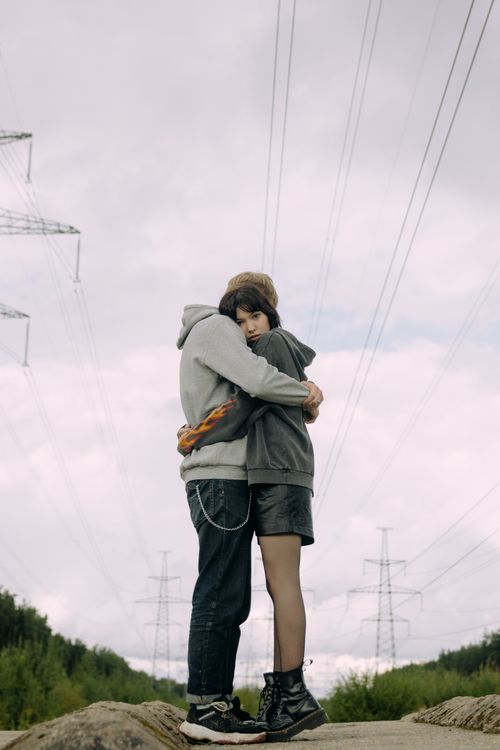 Free A young couple embraces under power lines, wearing casual streetwear. Moody sky overhead. Stock Photo