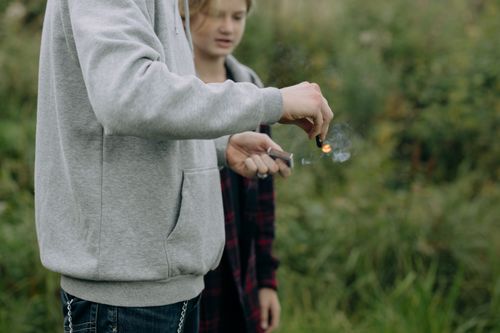 Free Teenagers outdoors lighting a firecracker with a matchstick. Captured in a natural setting. Stock Photo
