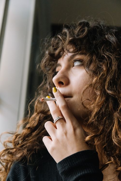 Free Portrait of a thoughtful woman with curly hair smoking indoors. Stock Photo
