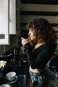 A woman with curly hair smokes a cigarette in a kitchen setting in Istanbul.