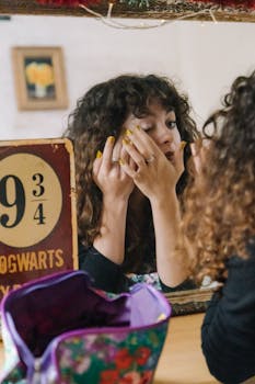 A woman with curly hair applies makeup, reflected in a mirror with Hogwarts sign.