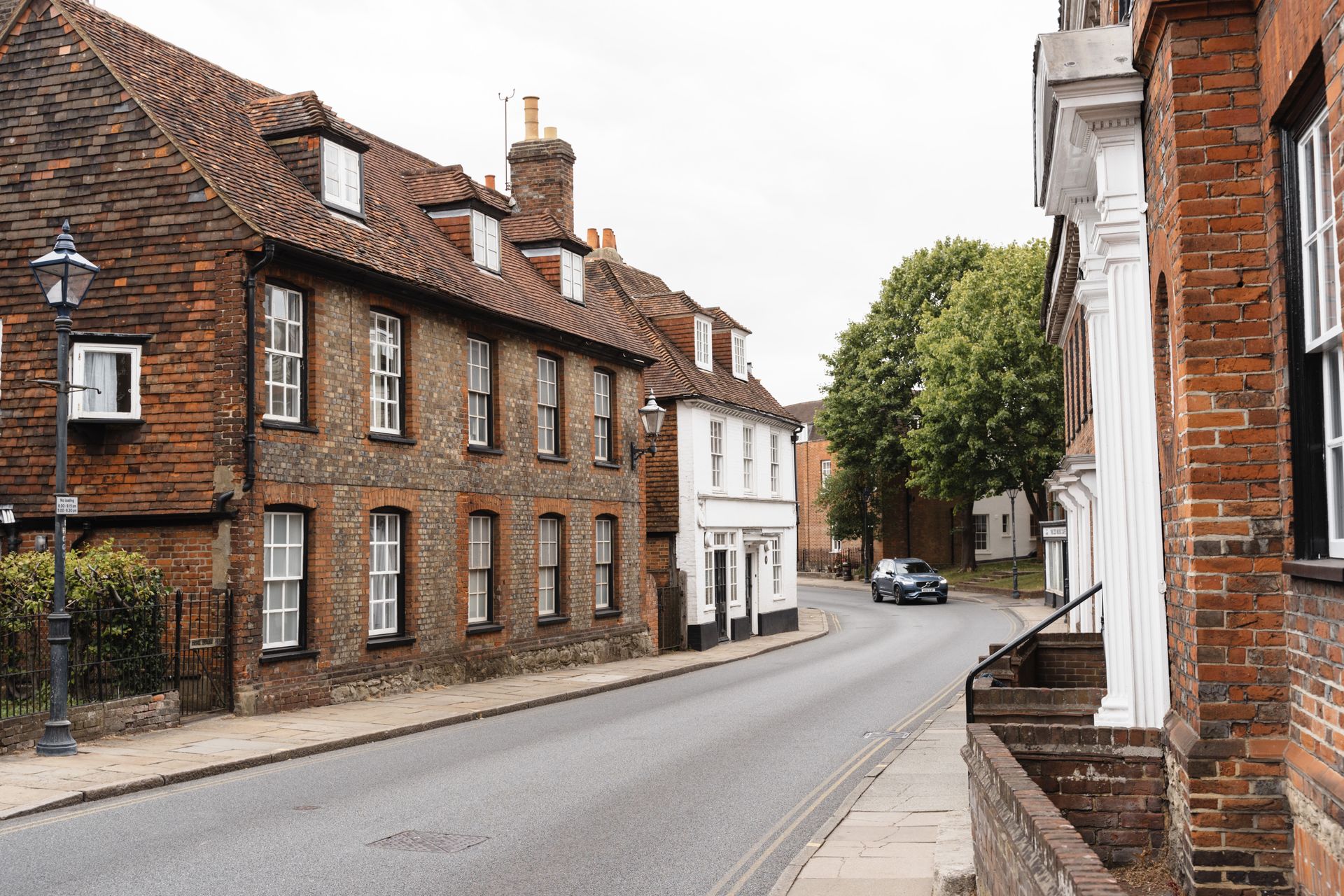 Scenic view of a quaint English village street with historic brick buildings and greenery.
