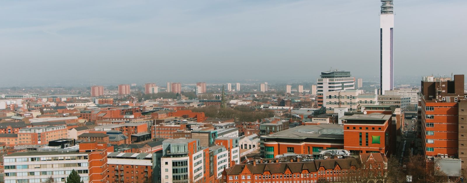 Tall industrial tower located amidst abundance of colorful residential houses with windows located on streets of city against blue sky