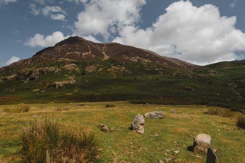 Free Grassy valley with stones located near green hills against cloudy blue sky in nature Stock Photo