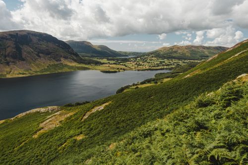 Free Hills covered with green grass and bushes located on shores of lake with peaceful water on cloudy day in countryside Stock Photo