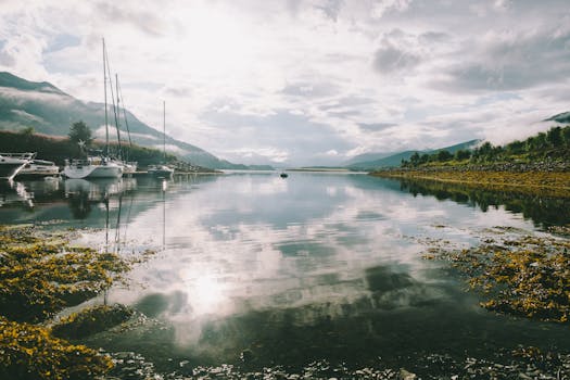 Peaceful reflection of boats and mountains at a Scottish lake, perfect for nature and travel imagery.