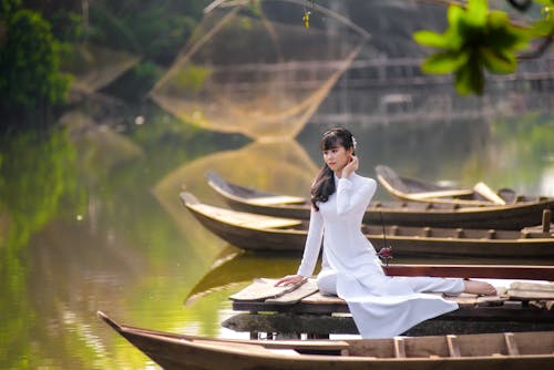 Woman in a White Ao Dai Posing Beside a Wooden Boat