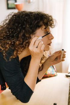 Young woman with curly hair applying mascara indoors in Istanbul, Turkey.