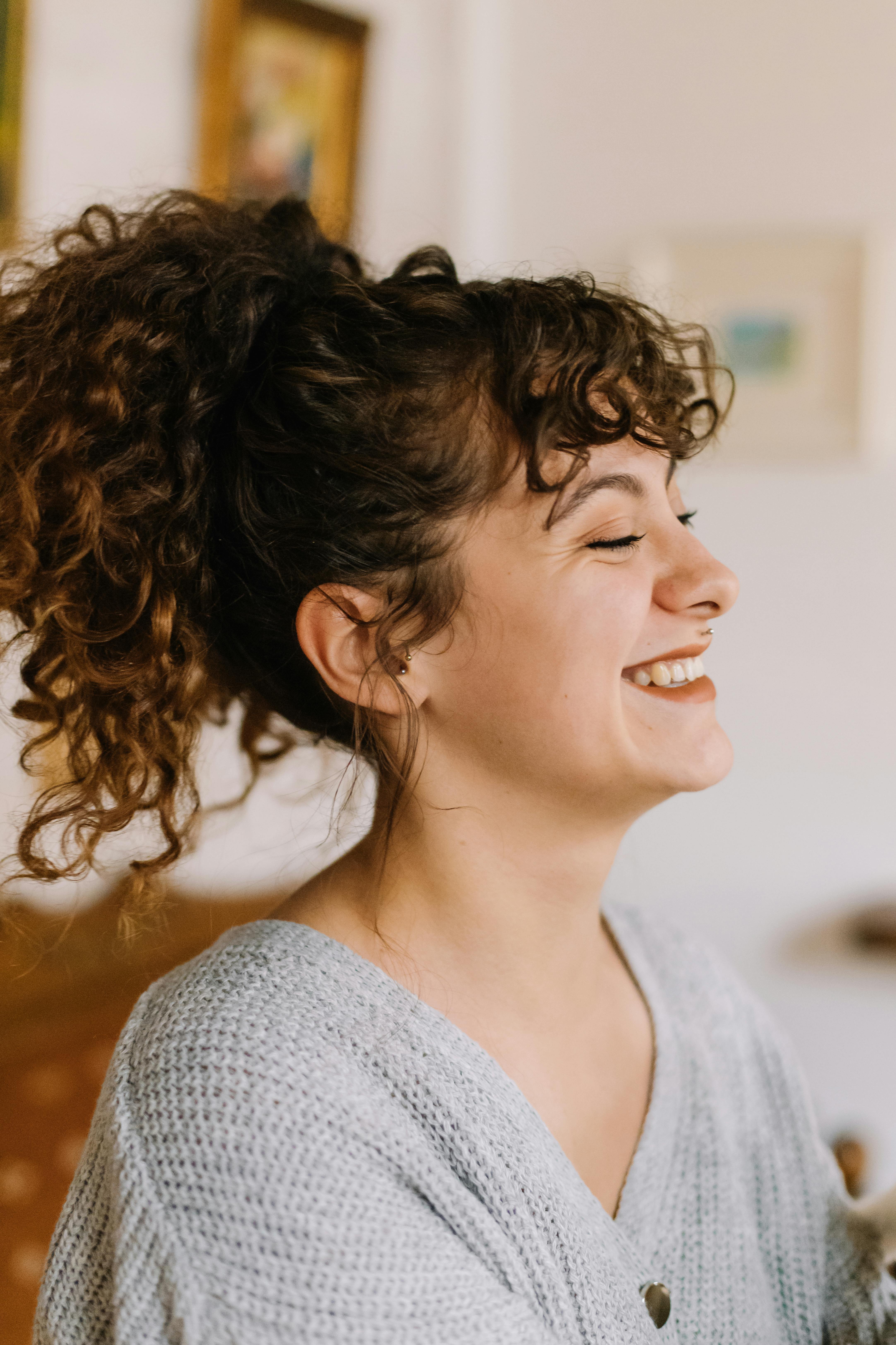 Portrait of a cheerful woman with curly hair smiling indoors in a cozy setting.