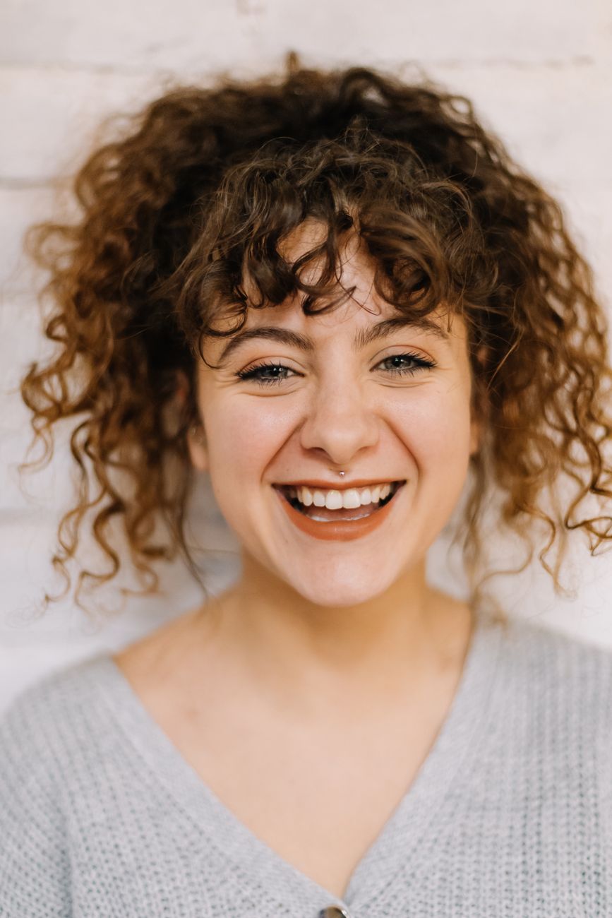 Portrait of a smiling woman with curly hair against a neutral background, captured in Istanbul.