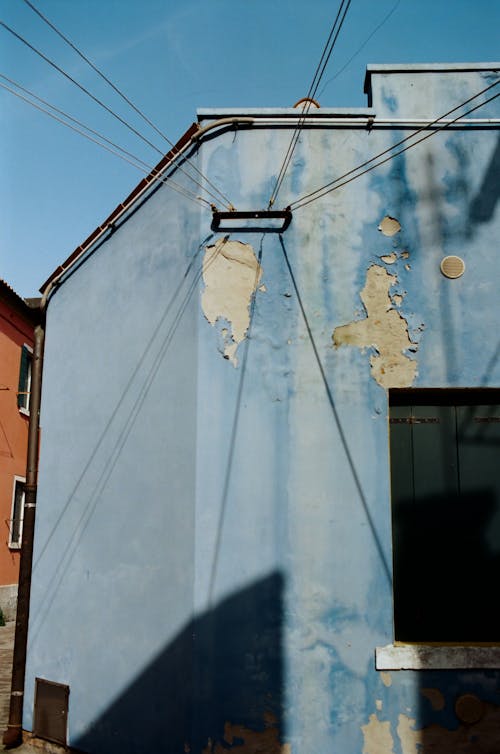 Exterior of old blue apartment building with cracked paints located in town district on sunny day