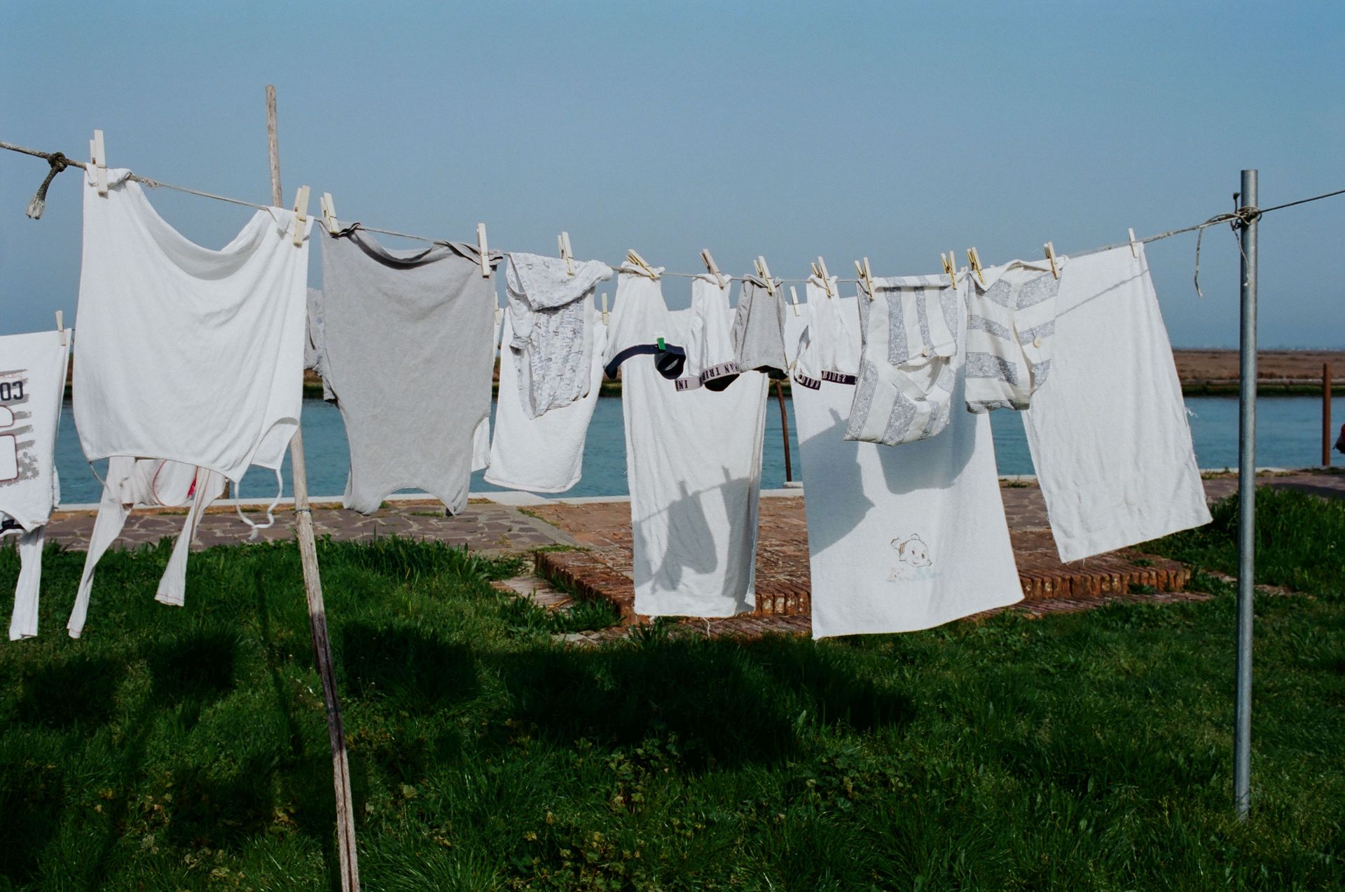 Drying washed laundry hanging on clothesline between poles on grassy seashore on sunny summer weather