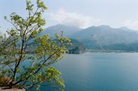 Picturesque scenery of blue sea rippling near rough rocky mountains and lush tree on sunny day