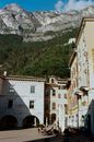 Historic old buildings with archways located on bottom of majestic massive mountain range under blue sky