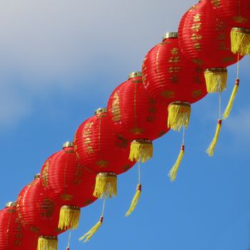 Row of red Chinese lanterns with gold accents hanging outdoors under a clear blue sky.（イメージ）