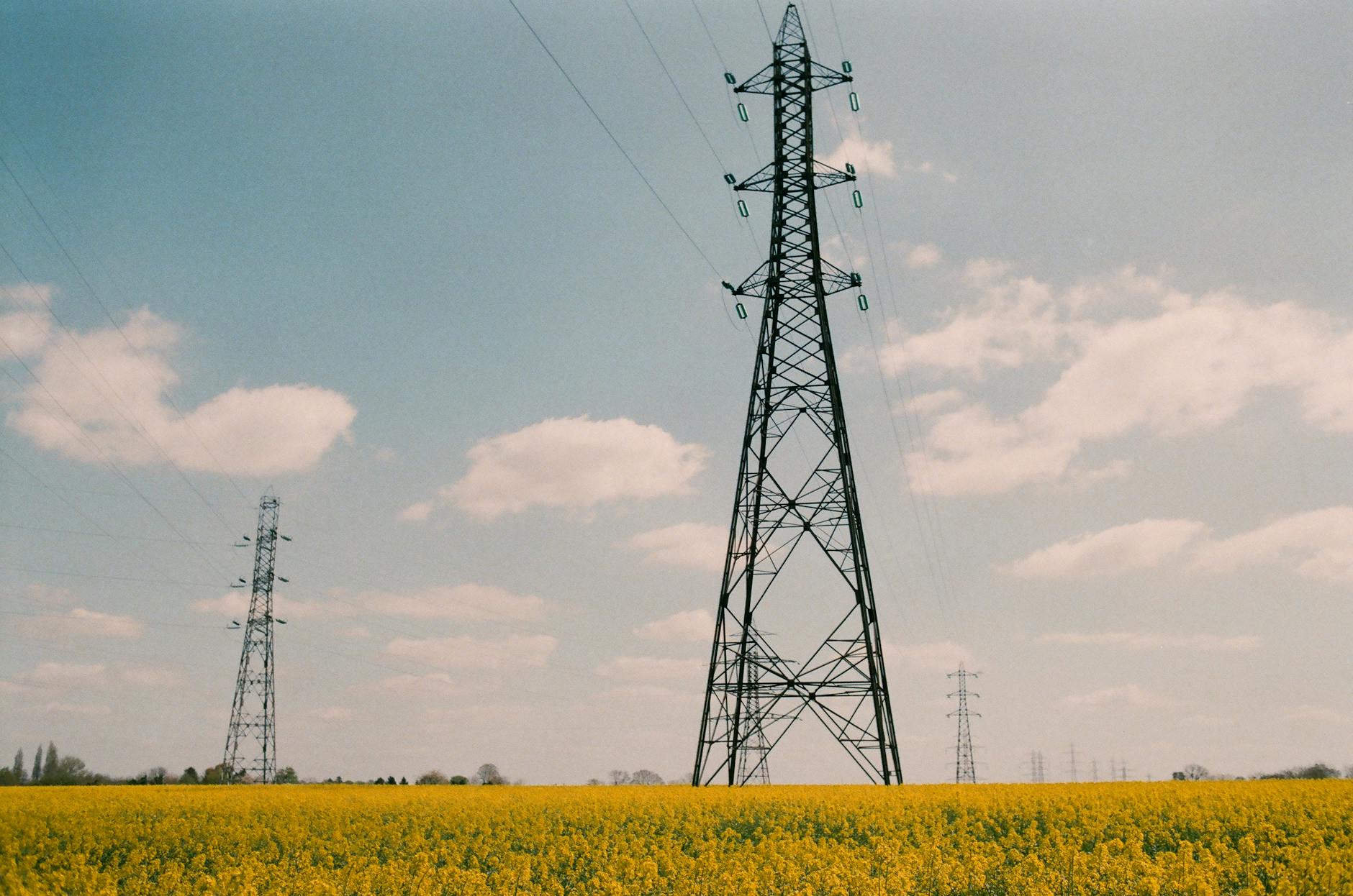 High voltage power lines set against a clear blue sky and a vibrant yellow meadow in rural France.