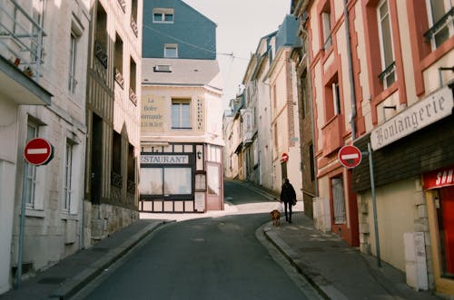 Distant man walking god on narrow walkway along road signs between aged residential houses with windows and signboards in town