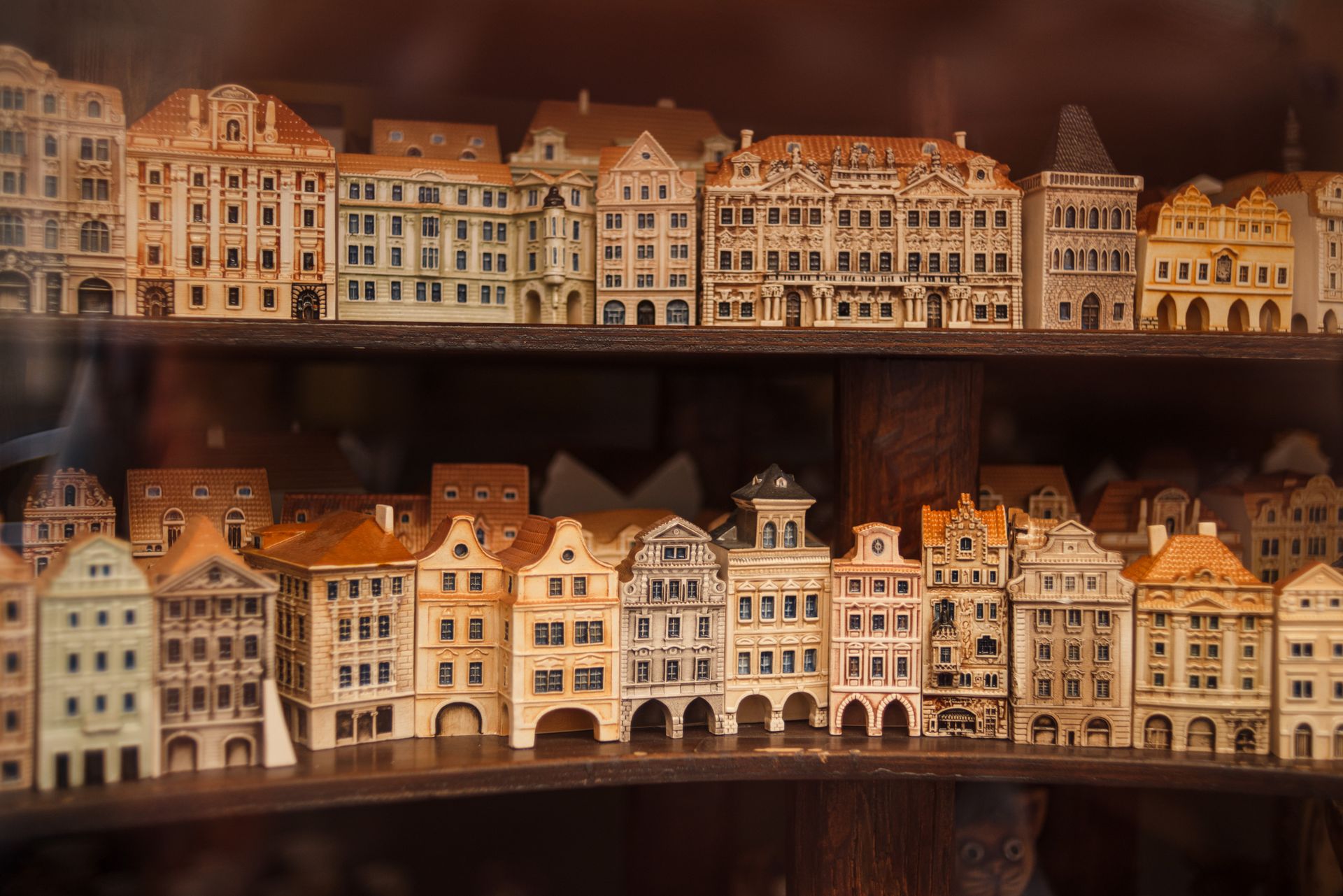 Through glass wall view of small building models with chimneys on roofs and arched doors on wooden shelves