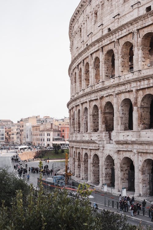 Colosseum exterior with arches against anonymous people and buildings under light sky in Rome Italy