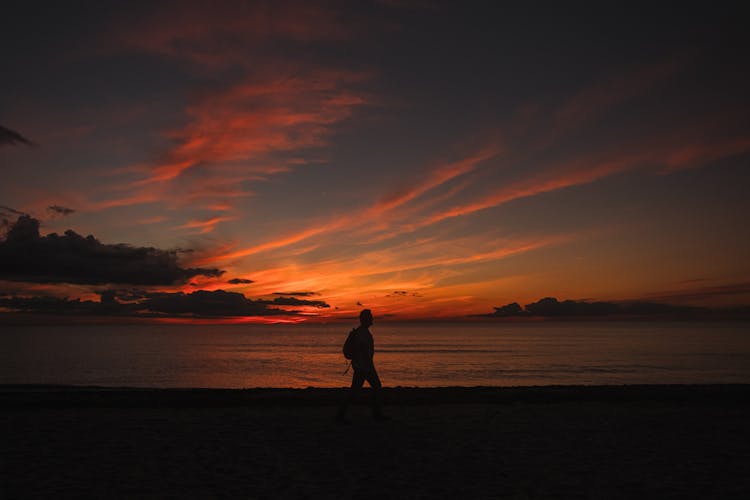 Anonymous Backpacker Silhouette Walking On Sea Shore Under Sunset Sky