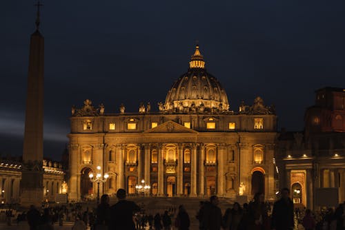 Old stone church with sculptures and columns against anonymous people at dusk in Vatican City Italy