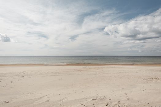 Scenery view of sandy shore against endless ocean under sky with fluffy clouds in daylight